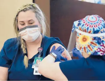  ?? SUE OGROCKI/AP ?? Hannah White, left, a registered nurse who works in the emergency room, becomes the first person in Oklahoma to receive Pfizer’s coronaviru­s vaccine Monday at Integris Baptist Medical Center in Oklahoma City. Public distributi­on of the shot is initially limited to front-line health workers and people in nursing homes and long-term care facilities.