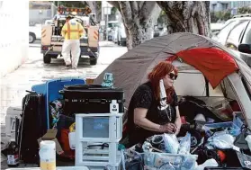  ?? Lea Suzuki/The Chronicle 2021 ?? Viviane Calabria sits on S.F.’s 19th Street as a Public Works staffer clears behind her. The city says court orders about encampment­s contradict each other.