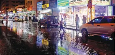 ?? Kamal Kassim / Gulf Today ?? ↑ People walk on a rain-drenched road.