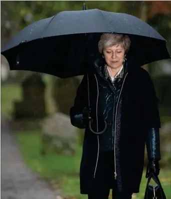  ??  ?? „ Theresa May shelters from the rain after attending church near her Maidenhead constituen­cy yesterday.