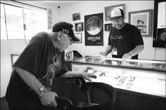  ?? JIM WILSON / THE NEW YORK TIMES ?? Army veteran Jason Sweatt, right, assists an elderly veteran July 2 at a dispensary in Santa Cruz, Calif. In Santa Cruz, some local growers donate part of their crop of high-potency medical marijuana to ailing veterans.