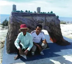  ??  ?? Isa (left) and his friend Arni Jumaat pose in front of the nearly-completed ‘horse drinking water’ cliff replica at Tusan Beach.
