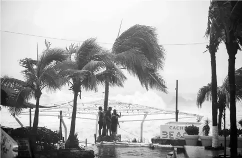  ??  ?? People stand next to swaying palm trees following the passing of Tropical Storm Lidia in Los Cabos, Mexico. — Reuters photo