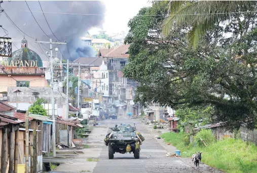  ??  ?? A government armored personnel carrier speeds away as black smoke billows from burning houses hit by rockets fired from military helicopter­s in the city of Marawi, on Tuesday. (AFP)