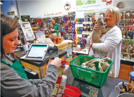  ?? STAFF PHOTOS BY DOUG STRICKLAND ?? Lacey Varnon’s dog, Harvey, licks her face as clerk Aleise Cline rings up her purchases at Nooga Paws on Small Business Saturday.