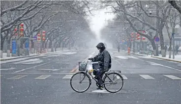  ?? (AFP) ?? A man wearing a mask rides a bicycle along a road as snow falls in Beijing on Wednesday
