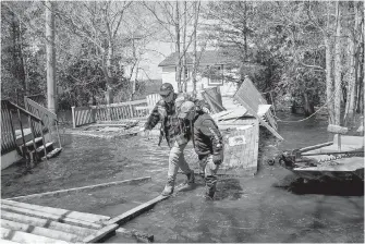  ?? PHOTOS BY DARREN CALABRESE, THE CANADIAN PRESS ?? Top: Kevin Gaddess, right, helps a friend navigate over debris from flooded homes and cottages on Route 690 in Princess Park,