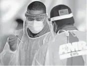  ?? DAVID SANTIAGO/AP ?? An American Medical Response health worker holds a swab after a person was tested at the COVID-19 drive-thru center at Holiday Park in Fort Lauderdale.