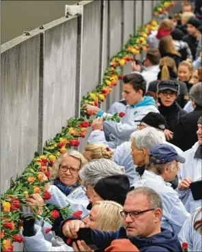  ?? SEAN GALLUP / GETTY IMAGES ?? People stick flowers into slats of one of the last portions of the Berlin Wall still standing at Bernauer Strasse following Saturday’s ceremony to celebrate the 30th anniversar­y of the fall of the wall Nov. 9, 1989.