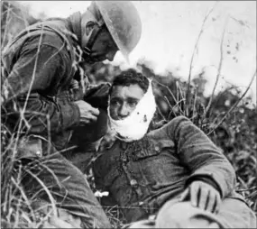  ?? PHOTO COURTESY OF THE NATIONAL ARCHIVES ?? An American soldier wraps another soldier’s head wound at Varennes-en-Argonne, France (September 1918).