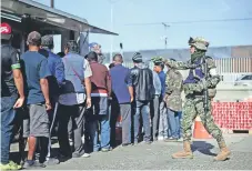  ??  ?? Los centroamer­icanos tienen que hacer largas filas para obtener un plato de comida, que preparan cocineros de la Marina; un oficial cuida el orden.