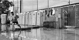  ?? REBECCA BLACKWELL/AP ?? Men bathe in a flooded shower and toilet area Thursday at a sports complex sheltering 6,150 Central American migrants, with 1,068 of those being children, in Tijuana, Mexico.