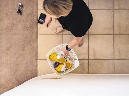  ?? ANTHONY JACKSON/JOURNAL ?? Buffy Mayerstein removes her shoes and loose items in her pocket before entering her living room. Whatever is placed in the bucket gets sanitized to protect her and her family after her shift at Lovelace Medical Center treating COVID-19 patients.