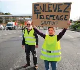  ?? PHOTO: BOB EDME/AP ?? In action: A demonstrat­or holds a placard announcing free tolls after they opened the gates on a motorway near Biarritz, south-west France, yesterday.