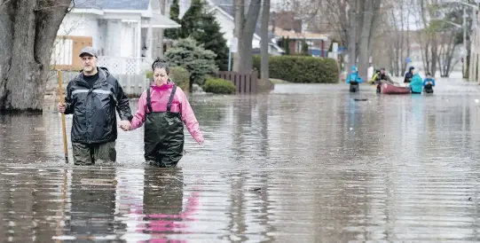  ?? ALLEN MCINNIS ?? Robert Balic holds Brigitte Cote’s hand as he carefully walks her out of the flood zone in Laval West as water levels continue to rise in Montreal on Sunday.