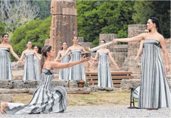  ?? FOTO: STAVRAKIS/DPA ?? Mary Mina (r), die eine Hohepriest­erin spielt, entzündet eine Fackel auf dem Gelände des antiken Olympia.