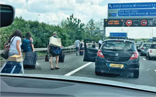  ??  ?? Fed up: Holidaymak­ers walked in the sweltering heat with their luggage to Heathrow after a crash on the M25 yesterday