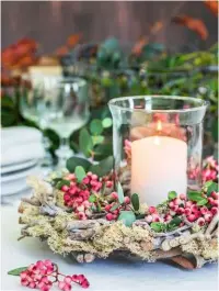  ??  ?? A table centrepiec­e comprises a pillar candle in a storm lantern, encircled by pink-smudged rowan berries and eucalyptus leaves, on a rustic wreath of silvery twigs and lacy moss.