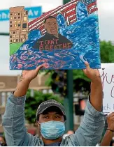  ??  ?? A protester in Minneapoli­s holds a painting of George Floyd.