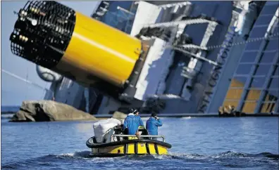  ?? FILIPPO MONTEFORTE, Afp/getty Images, file ?? A January photo shows technician­s in a small boat passing near the stricken cruise liner Costa Concordia lying aground after hitting underwater rocks on Jan. 13. Owner Carnival Corp. significan­tly cut its financial
forecast on Friday.