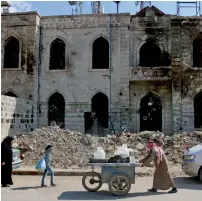 ?? AFP ?? A street vendor pushes a cart carrying plastic liquid containers down a street past the damaged courthouse building in the city of Azaz, on Syria’s northern border with Turkey. —