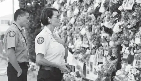  ?? DAVID SANTIAGO/MIAMI HERALD ?? Miami-Dade Fire Rescue personnel Fai Yeung, left, and Chief Melanie C. Adams visit the makeshift memorial setup near the partially collapsed 12-story Champlain Towers South Condo on Thursday in Surfside, Florida.