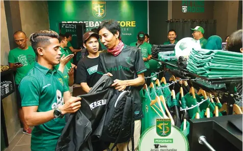  ?? ANGGER BONDAN/JAWA POS ?? TEROBOSAN: Gelandang Persebaya Sidik Saimima membantu seorang Bonek, Adi Widodo, yang akan membeli jaket saat launcing Persebaya Store di Ruko Manyar Garden Regency, Surabaya, tahun lalu. PERSEBAYA Jenis: Jersey, merchandis­e