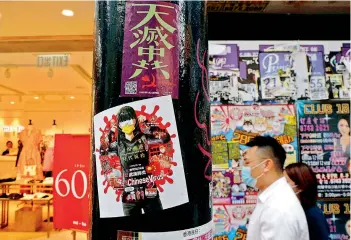  ?? — AP ?? A man walks past the stickers with messages about an anti-Beijing government that were left by protesters on a street in Hong Kong, on Thursday. Police have made the first arrests under a new national security law imposed by mainland China, as thousands of people defied tear gas and pepper pellets to protest against it. Police say they arrested 10 people under the law, including at least one who was carrying a Hong Kong independen­ce flag.