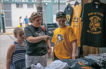  ?? Alex Caprara/Post-Gazette ?? Jodi Dague, along with her son Connor and daughter Cassie, dons her Penguins apparel while reading the back of a T-shirt for sale Friday in the Strip District.