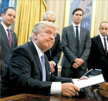  ?? Evan Vucci/Associated Press ?? President Donald Trump signs the last of three executive orders Monday in the Oval Office. Standing, from left to right: White House Chief of Staff Reince Preibus; Peter Navarro, director of the National Trade Council; and Jared Kushner and Steven...