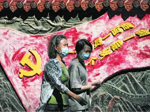  ?? AP ?? Mujeres con mascarilla pasan por un mural del partido comunista en Pekín, China