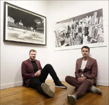  ?? Charles Rex Arbogast/Associated Press ?? Chicago Cubs left fielder Ian Happ, left, and British artist Pat Vale sit for a portrait under Vale’s work titled “See What I See, Pat Vale With Ian Happ,” of views that Happ sees at Wrigley Field on the field and Vale’s cityscapes, a joint venture with Happ’s charity at the Gallery Victor on June 16 in Chicago.