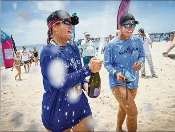  ?? PHOTOS BY MELANIE BELL / THE PALM BEACH POST ?? Shelly Griffith (left) opens a bottle of champagne next to her twin sister, Sherry Griffith, after their team of four called Crewcial Sirens finished their paddle in a 300-pound dory surfboat.