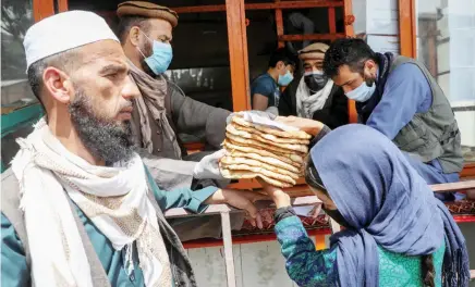  ?? File/Reuters ?? An Afghan girl receives free bread — distribute­d by the government — outside a bakery in Kabul amid preventive measures against the coronaviru­s.