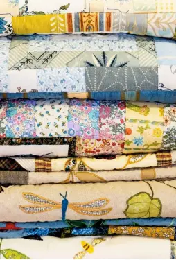  ??  ?? A stack of finished quilts. Some have floral patches or panels in complement­ary fabrics and others feature appliqués drawn from nature.