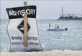  ?? Allen J. Schaben Los Angeles Times ?? AN ADVISORY cautions beachgoers near Belmont Shore as Cal State Long Beach researcher­s look for several sharks reported in shallow water in May.