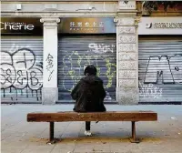  ?? Ansa ?? Serrande abbassate Un cittadino milanese su una panchina di fronte ai negozi chiusi di via Paolo Sarpi