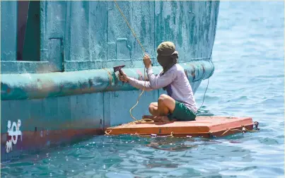  ?? (SUN.STAR FOTO/ALLAN CUIZON) ?? COAT. A worker holds on to a rope as he chips off rust from the hull of a boat before applying a fresh coat of paint.
