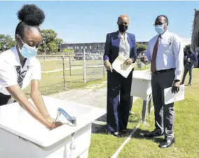  ??  ?? Education Minister Fayval Williams and Dunoon Park Technical High School Principal Shawn Aarons watch as student Jadon Simpson washes her hand on entering the school compound yesterday for the resumption of face-to-face classes.