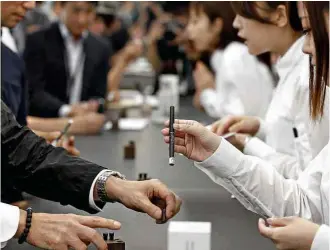  ??  ?? Vendedoras japonesas explicam para clientes como o cigarro eletrônico funciona