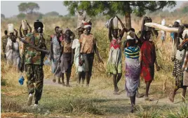  ?? (Siegfried Modola/Reuters) ?? A SOLDIER WALKS past women carrying their belongings near Bentiu, South Sudan, in February.