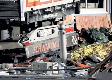  ??  ?? NIGHTMARE BEFORE CHRISTMAS: A gold-foil rescue blanket covers a body lying amid the wreckage left by a truck at an outdoor Christmas shopping market in Berlin’s Breitschei­dplatz square on Monday.