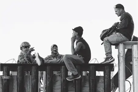  ?? Gregory Bull / Associated Press ?? U.S. Border Patrol agents, left, speak with two Central American migrants Wednesday as they sit atop the border structure separating Mexico and the United States in Tijuana, Mexico. Nearly 600 agents from Texas as been sent to California.