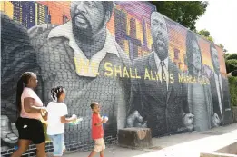  ?? RYON HORNE/THE ATLANTA JOURNAL-CONSTITUTI­ON PHOTOS ?? A family walks past a mural of civil rights leaders painted on the side of Privado barbershop.