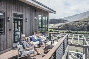  ??  ?? Mark, Alena and Vicci Kane sit on the top-floor deck of their getaway home with dogs Toula and Tippet, overlookin­g a community-owned vineyard, the Yakima River and the railroad tracks that run alongside it. “It seems very quiet except when the train goes by,” says Vicci.