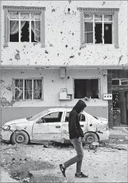  ?? ASSOCIATED PRESS] [LEFTERIS PITARAKIS/THE ?? A youth walks past a house and a car damaged by a rocket in the town of Kilis, Turkey, near the Syrian border.