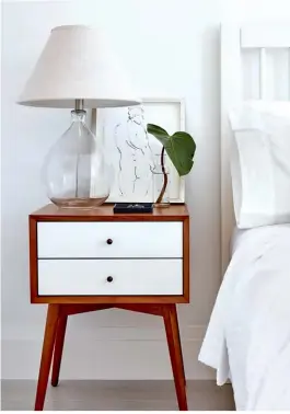  ??  ?? ABOVE, RIGHT This two-toned wooden Mid-Century Modern nightstand with quirky splayed legs injects a dose of playfulnes­s and warmth into the otherwise all-white space.