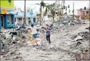  ?? AP PHOTOS ?? Left, boats lie scattered amid mobile homes in the San Carlos area of Fort Myers Beach. Right, Jake Moses, 19, left, and Heather Jones, 18, of Fort Myers, explore a section of destroyed businesses at Fort Myers Beach.