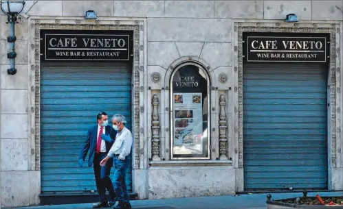  ?? (AFP) ?? Men wearing a face mask walk past a closed restaurant on Via Veneto in central Rome recently.