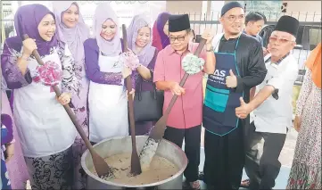  ??  ?? Sharifah Hasidah (left) and Juita (third left) join other Kampung Sungai Bedil folk in stirring the ‘bubur lambuk’ prior to the distributi­on.